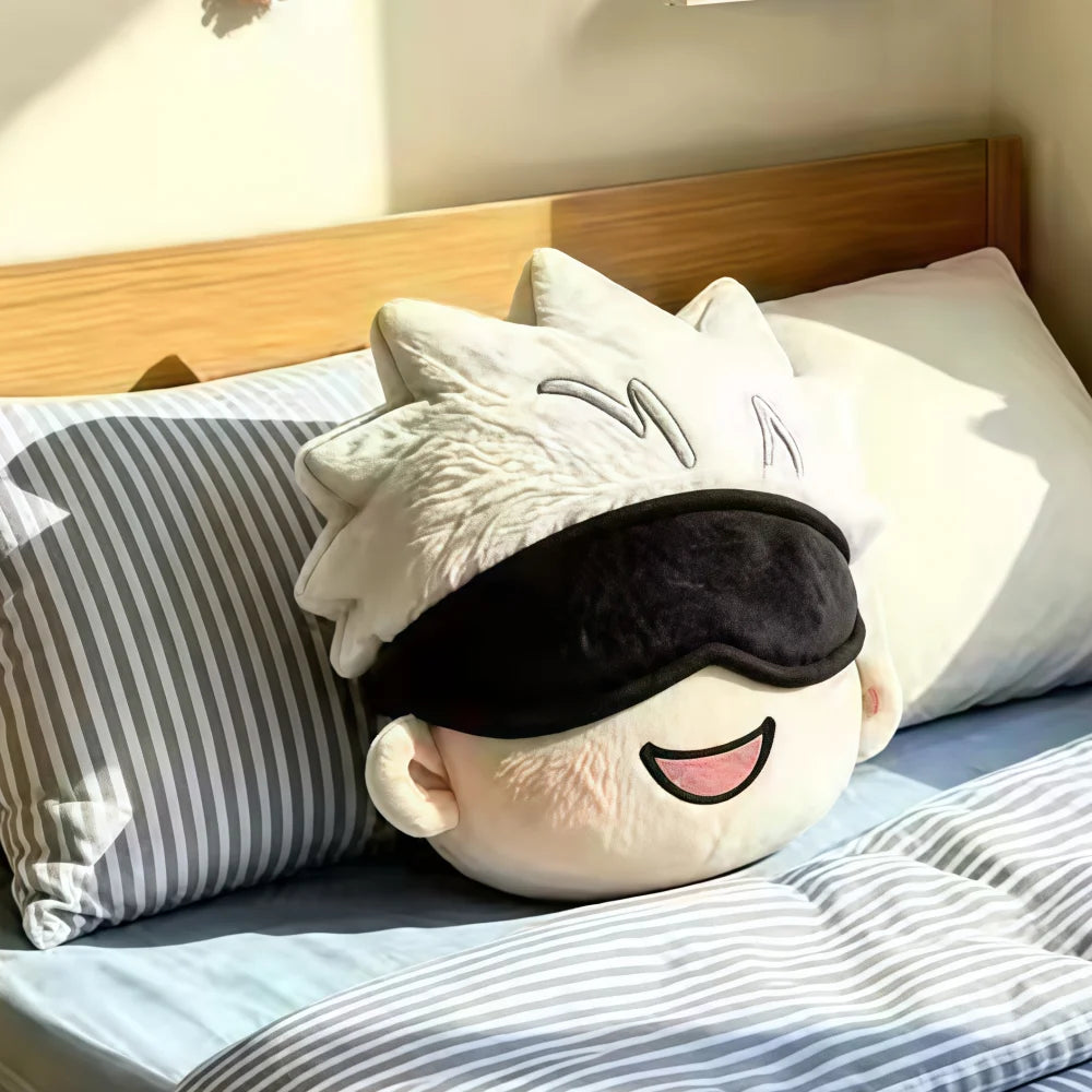 A plush character pillow with spiky white hair and a black sleep mask, resting on a bed with striped pillows and blue bedding.